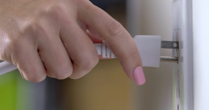 Woman's hand plugs an electric cord into a wall outlet in the United States. Recorded in 4K with dolly move from right to left.