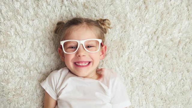 Pretty smiling  girl wearing glasses thinking of new idea and laughing. Cute kid on the floor at home. 