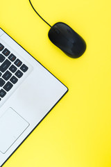 The wired computer mouse and the laptop are isolated on a yellow background. Flat lay template for...
