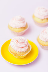 Cupcake decorated with pink buttercream in bright yellow plate on pastel pink background. Sweet beautiful cake. Vertical banner, greeting card, congratulation. Close up photography. Selective focus