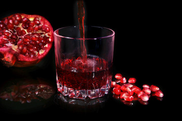 Glass with pomegranate juice Pomegranate seeds and Beautiful ripe pomegranate on black mirror background with place for copy space.