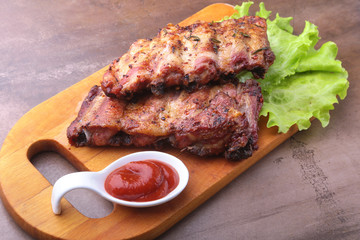 grilled barbecued ribs with lettuce leaves, hot chili pepper and sauce on wooden cutting board.