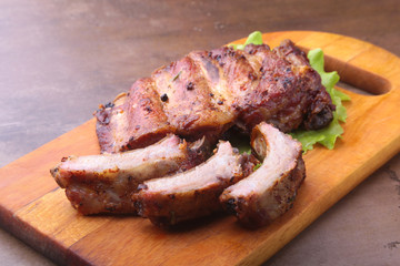 grilled barbecued ribs with lettuce leaves, hot chili pepper and sauce on wooden cutting board.