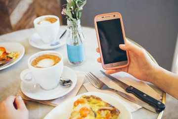 Woman leaning on the table in cafe and text messaging with her mobile, hands close up. Having breakfast, drinking coffee and eating french quiche and reading news from internet. Copy space area.