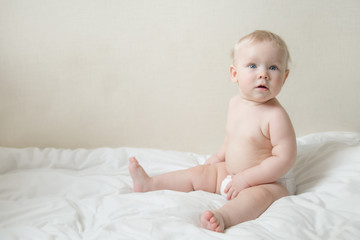 Beautiful surprised cute blonde baby girl with blue eyes on the bed in the  bedroom. Happy child.  place for text.