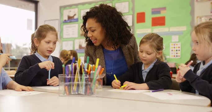 4K Primary school children drawing in the classroom with teacher helping. Slow motion