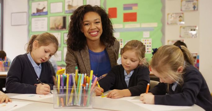 4K Portrait smiling school teacher in class with young children drawing pictures. Slow motion