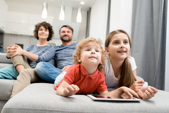 Portrait Of Happy Family With Two Kids  Watching TV Together Sitting On Sofa In Living Room, Focus On Brother And Sister In Foreground