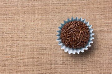 Brigadeiro is a chocolate truffle from Brazil. Cocoa and sprinkles of chocolate. Children birthday party sweet. Flat lay design of candy ball over wood.