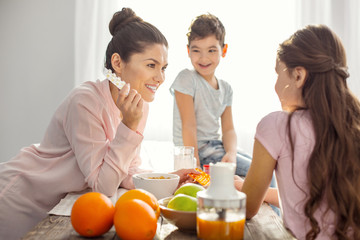 Good vitamins. Attractive smiling dark-haired young mother holding vitamins and talking with her kids about healthcare and the boy sitting on the table