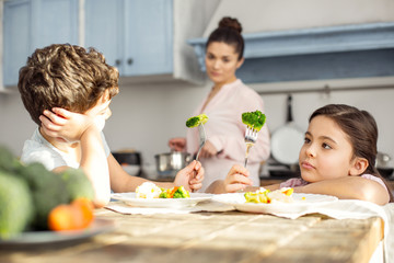 Tasty vegetables. Pretty concentrated dark-haired little girl having breakfast with her brother and...