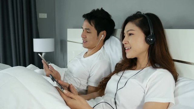 4k of young couple listening music from mobile with headphone on bed