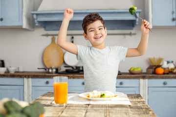 I am strong. Handsome cheerful dark-haired little boy having healthy breakfast and smiling and...