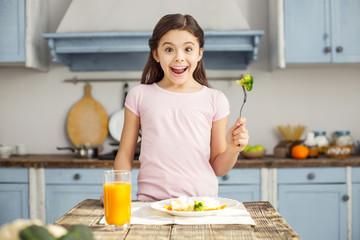 I am healthy. Beautiful exuberant dark-haired little girl smiling and having healthy breakfast and drinking some juice