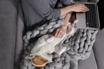 Cozy home, woman covered with warm blanket watching movie, Dog sleeping on female feet. Relax, carefree, comfort lifestyle.