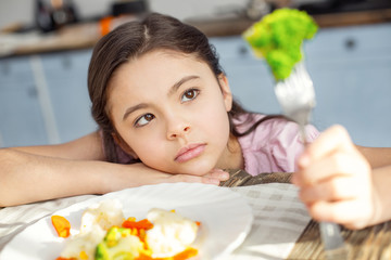 I feel sad. Pretty sad dark-haired little girl having healthy breakfast and looking at the green...