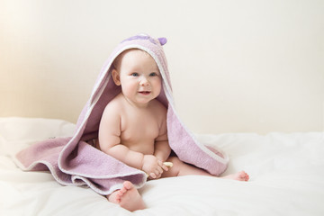  little girl sits on the bed in the bedroom after a shower. baby with a towel on head. ready for bed. concept of a happy family. place for text.