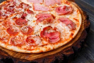 Hot fresh pizza with bacon, salami,ham and pepperoni, close up. Italian food, restaurant or pizzeria concept