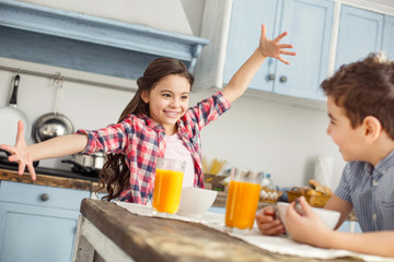 Telling a story. Attractive content little dark-haired girl smiling and talking with her brother while they having breakfast