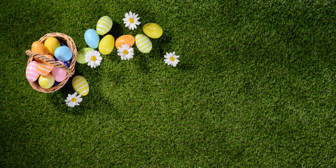 Obraz premium above top view of multi colored painted easter eggs on the green grass with springtime daisy flowers