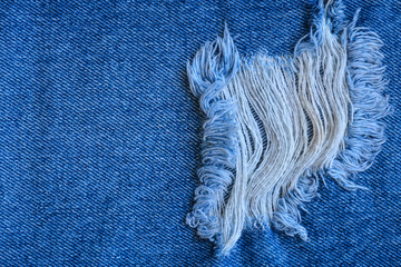 Fragment of jeans trousers with torn, ripped patch, decorated with a hole with threads. Denim background.