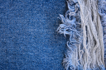 Fragment of jeans trousers with torn, ripped patch, decorated with a hole with threads. Denim background.