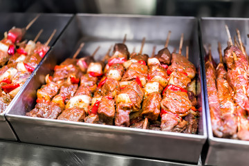 Marinated pink red raw beef meat kebabs on wooden sticks, vegetables, onions, peppers in store display, metal trays for sale