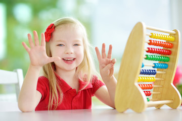Cute little girl playing with abacus at home. Smart child learning to count.