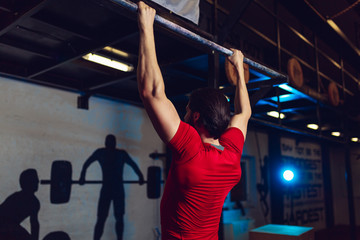 Muscular bearded male doing exercises on horizontal bar in a gym club.