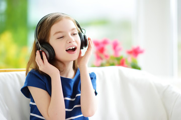 Cute little girl wearing huge wireless headphones. Pretty child listening to the music. Schoolgirl having fun listening to kid's songs at home.