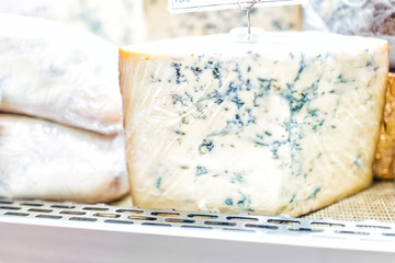 Macro closeup of blue cheese chunk hunk large piece wrapped in plastic wrap on display sale in store grocery supermarket shop gourmet showing mold