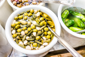 Closeup of plastic container jar filled with bulk green pickles gherkins, garlic, olives, cornichon in vinegar brine