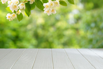 Empty white table with a blurred green background. White wooden table in the background of a summer garden. A branch of blossoming jasmine.