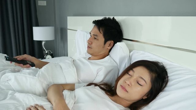 4k of young couple lying on a bed with remote control and watching television in the bedroom