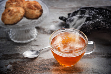 hot tea with steam in a glass cup on a wooden table, cookies and snowy gloves blurred in the background, best warm up after a winter walk, selected focus, narrow depth of field