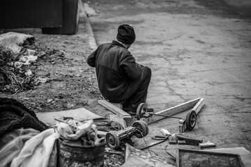Poor man sitting on sidewalk near heap of garbage outdoors