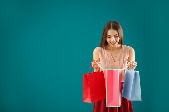 Young woman with shopping bags on color background