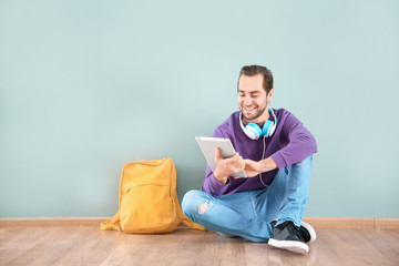 Student with tablet sitting on floor against color wall