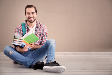 Student with notebooks sitting on floor against color wall
