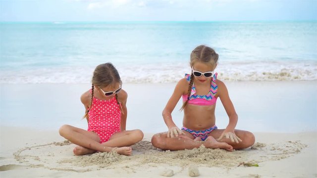 Adorable little girls have a lot of fun on the beach. Two beautiful kids playing with sand on the seashore