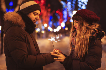 Young loving couple holding sparklers outdoors on winter evening