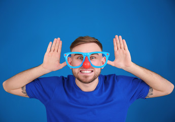 Young man in funny disguise posing on color background. April fool's day celebration