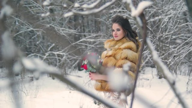 Beautiful bride in a fur coat in a winter pine forest with a wedding bouquet
