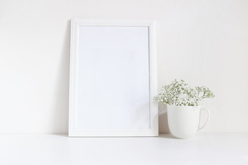 White blank wooden frame mockup with baby breath, Gypsophila flowers in porcelain mug on the table. Poster product design. Styled stock feminine photography. Home decor.