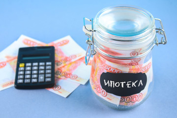 Bank with Russian money, 5000 rubles and a calculator on a gray background. Finance, moneybox, education. Text in Russian: mortgage.
