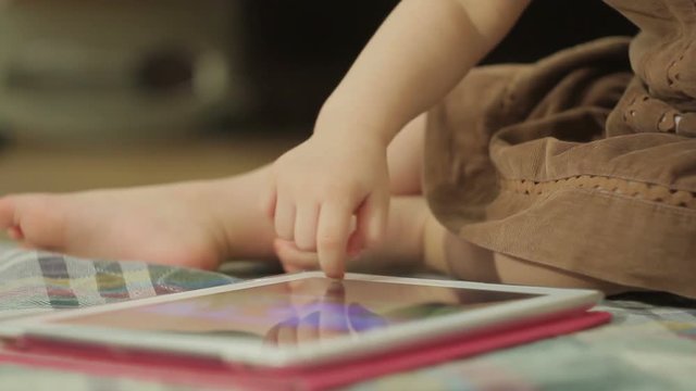 A little girl sitting on the floor uses a tablet PC, touching her finger on the touch screen