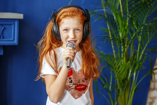 A red-haired little girl sings a song. The concept is childhood, lifestyle, music, singing, listening, hobbies.