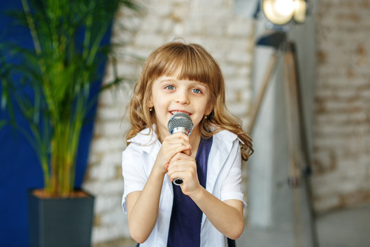 A little beautiful girl sings in a microphone. The concept is childhood, lifestyle, music, singing, listening, hobbies.