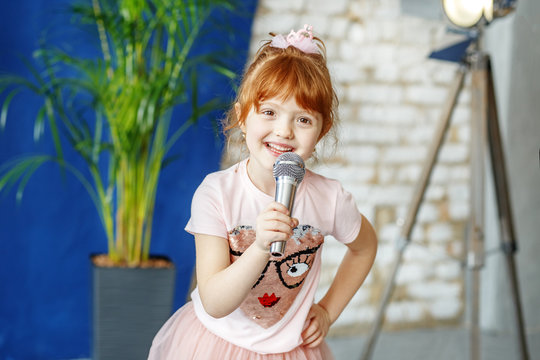 Smiling child sings a song into the microphone. The concept is childhood, lifestyle, music, singing, listening, hobbies.