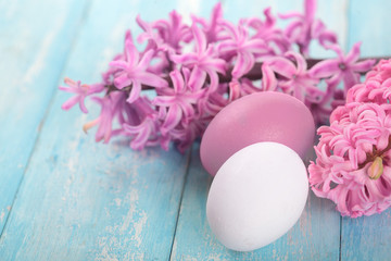 Easter eggs white and purple on a cyan wooden table.Flower hyacinth in bucket.Copy space.Easter background.Closeup Selective focus .Spring time.Violet toned